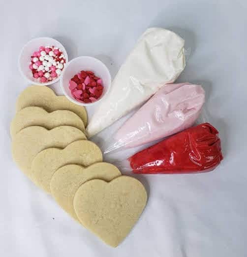 6 hear shaped cookies, 3 bags of frosting and 2 sprinkles in valentine colors