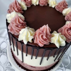 neapolitan cake, with pink Champagne vanilla and chocolate layers, a ganache drip, and buttercream swirls on top